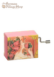 Rectangular music box with silver hand crank extruding from the side.  The box is pink with a soft stylized painting of a lady smelling a rose.