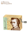 A rectangular music box with a silver hand crank extruding from the side. The box shows a sepia photo of Mozart with his name depicted. 