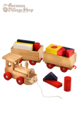 A pine wooden train with red wheels, pulls two rectangular carriages full of colourful building blocks.