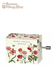 Rectangular music box with silver hand crank extruding from side. Box is white with red and pink flowers. The text on the box says "Maria Sibylla Merian"